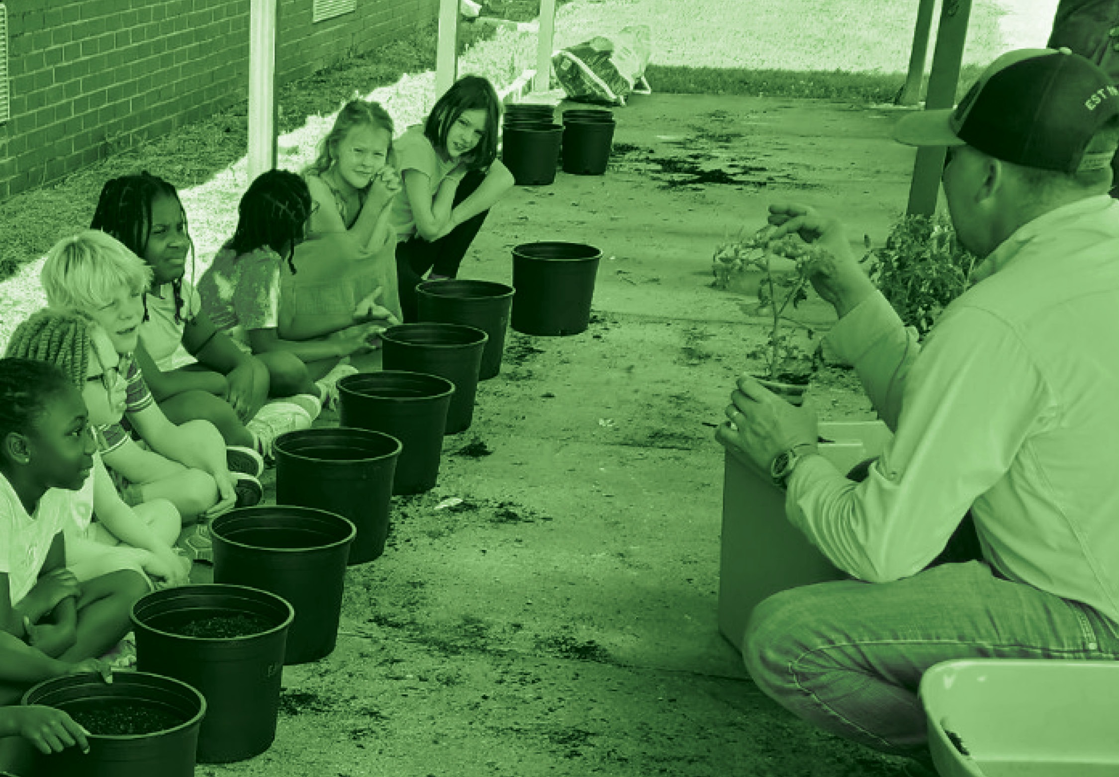 adult man holding plant teaching onlooking children about planting trees