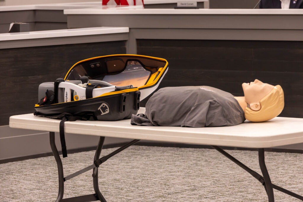 A LUCAS Device in its transport bag sitting on a table next to a CPR dummy