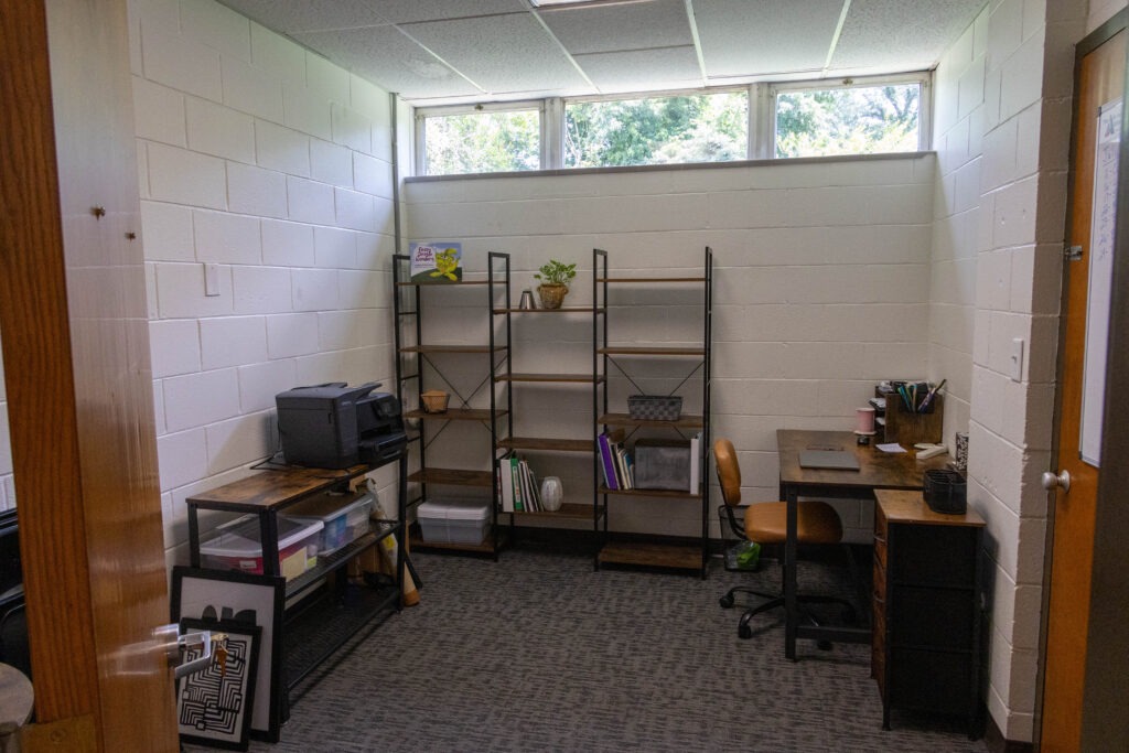 An office in use with a desk, shelving, plants, and office materials