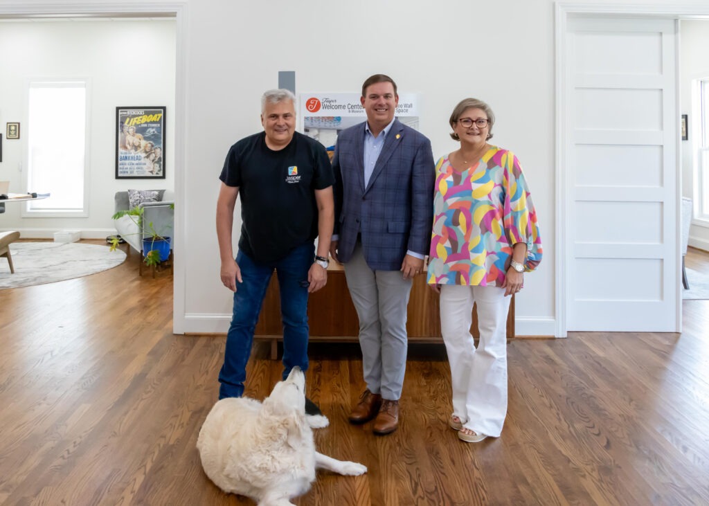 Sen. Matt Woods poses with Mike Putnam and Renae WIlson at the front of the Jasper Main Street Welcome Center. A golden retriever lays in front of them