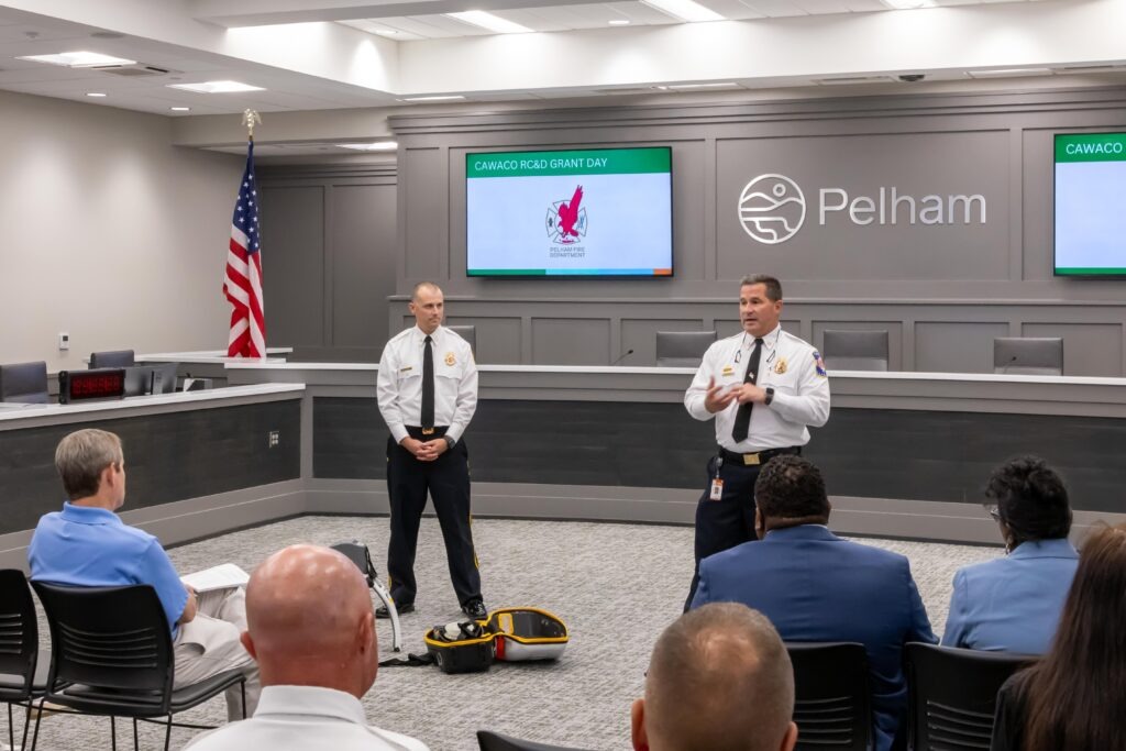Matt Maples and Mike Reid stands at the front of the room and talks about the City of Pelham's project. A LUCAS device is on the floor on display