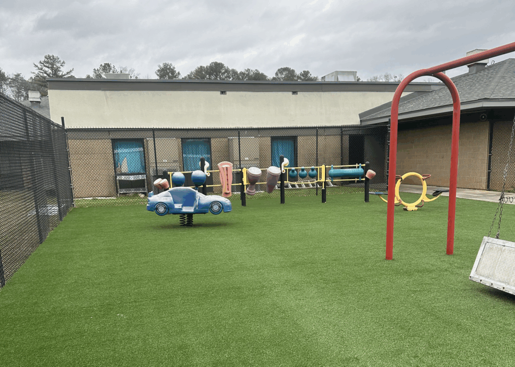A fenced-in playground behind a school with fresh green turf