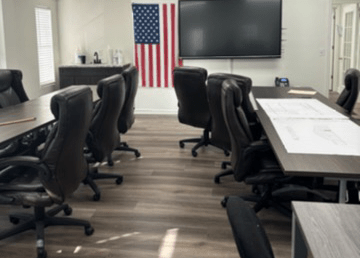 An office space with three conference tables, several office chairs, a mounted TV at the front of the classroom, and an American flag