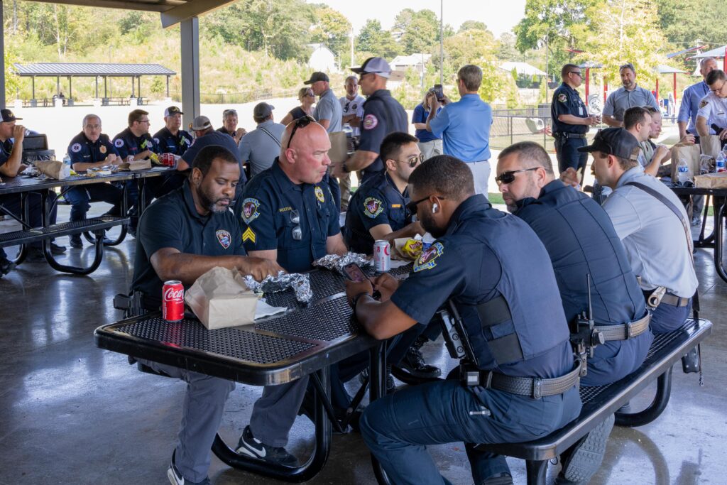 Police officers in uniform sitting at picnic tables eating lunch and other attendees mingling throughout the covered area.
