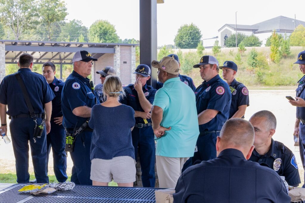 Rep. Leigh Hulsey and Rep. Kenneth Paschal speak to a group of uniformed officers under a shaded pavilion