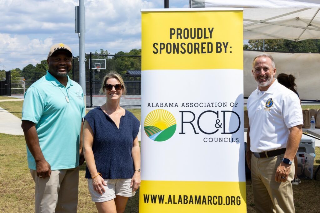 Rep. Kenneth Paschal, Rep. Leigh Hulsey, and Rep. Russell Bedsole pose next to an Alabama RC&D sponsorship banner