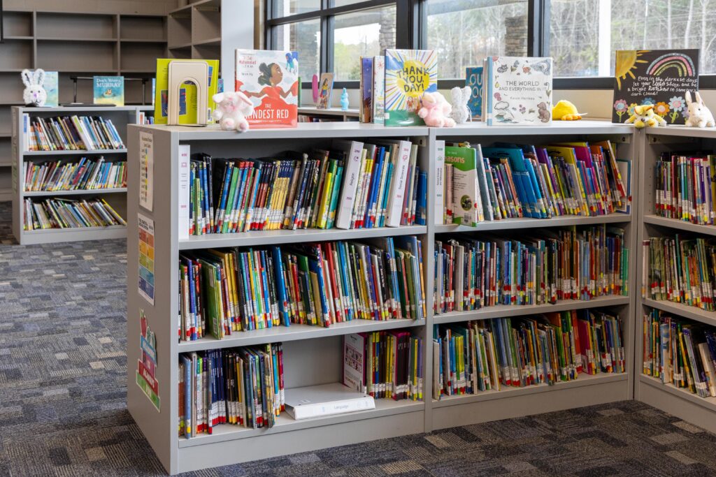 New shelving units filled with colorful books in Lupton Junior High's renovated library, with featured titles displayed face-out on top of the shelves alongside decorative stuffed animals.