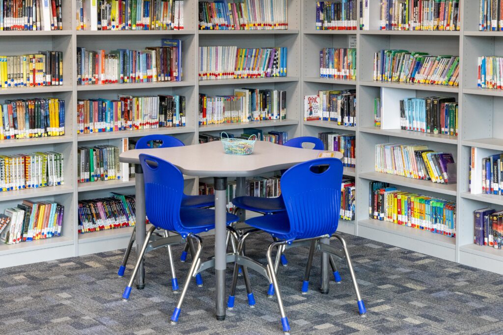 A small student workstation with four blue chairs sits tucked into an alcove of floor-to-ceiling bookshelves filled with colorful books in Lupton Junior High's renovated library.