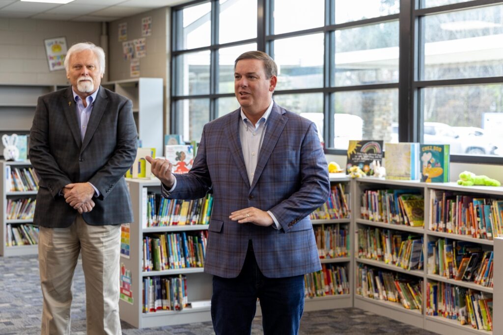 Sen. Matt Woods addresses attendees during the Lupton Junior High library grant announcement, with Rep. Greg Barnes standing alongside him, surrounded by the school's newly renovated bookshelves.