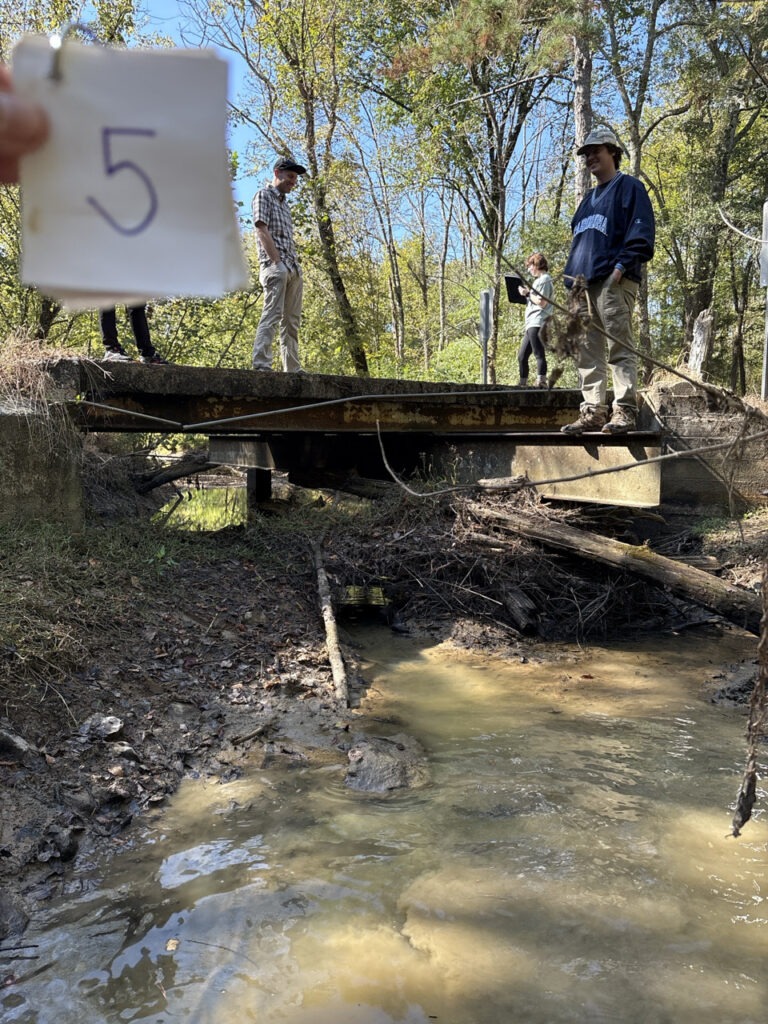 Geological Survey of Alabama staff and Auburn University student interns stand beside a deteriorating stream crossing structure during a field training session for Stream Crossing Assessments in the Ballplay Creek watershed.