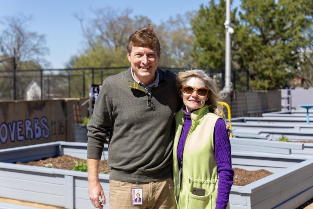 Michelle Barnes and Frank Long stand together smiling among the new raised garden beds on the Lovelady Center rooftop on a sunny day.
