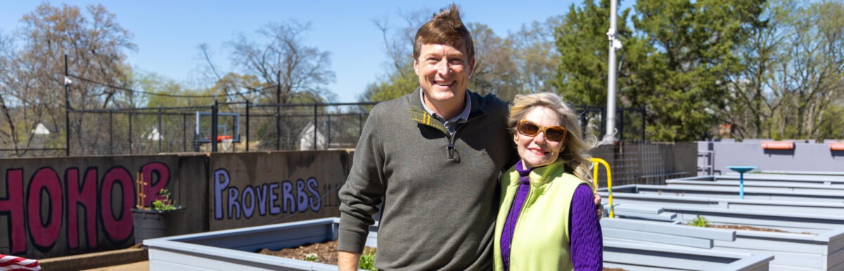 Michelle Barnes and Frank Long stand together smiling among the new raised garden beds on the Lovelady Center rooftop on a sunny day.