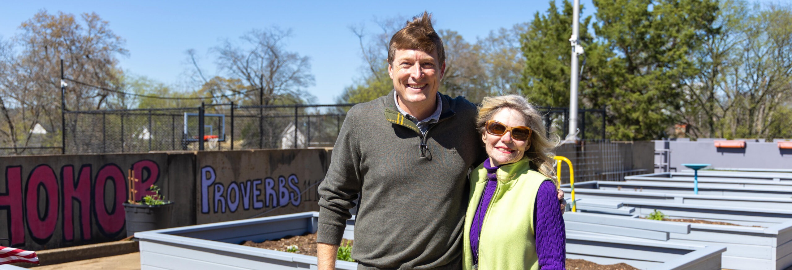 Michelle Barnes and Frank Long stand together smiling among the new raised garden beds on the Lovelady Center rooftop on a sunny day.