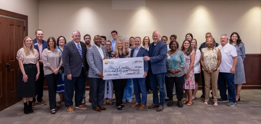 Legislators and grant recipients pose in a Calera City Hall meeting room. Four legislators in the center hold an oversized check from Cawaco RC&D to Shelby County for $144,950 with the memo "2026 Grants."