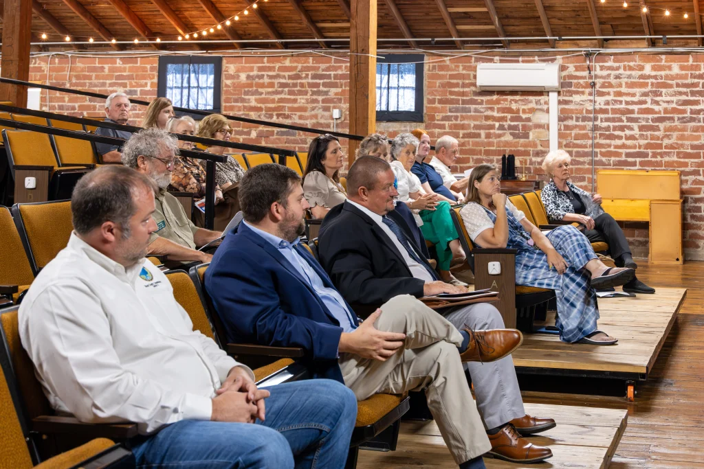 Legislators and community members sit in tiered, gold theater seats inside the brick-walled Community Arts Council building, listening to remarks during Grant Day.